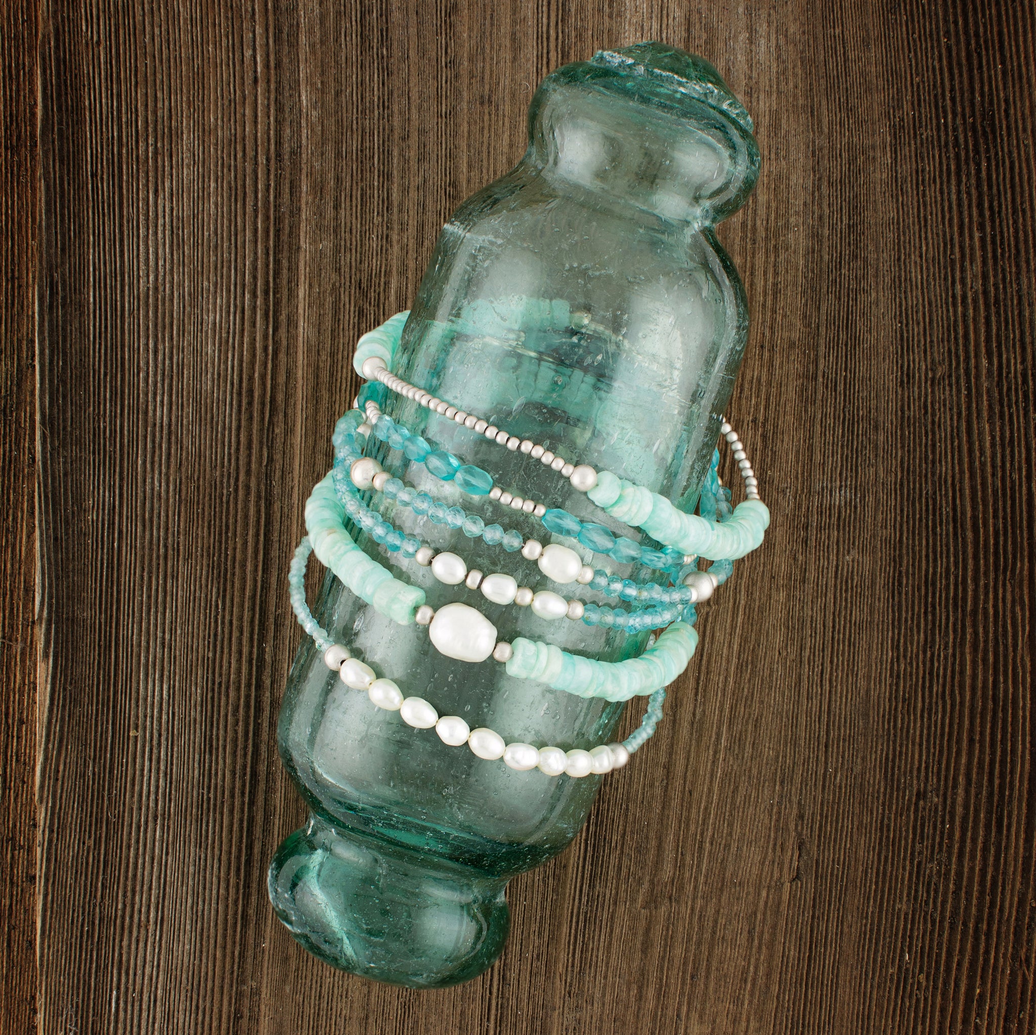 Turquoise glass bottle with beaded bracelets on a wooden surface